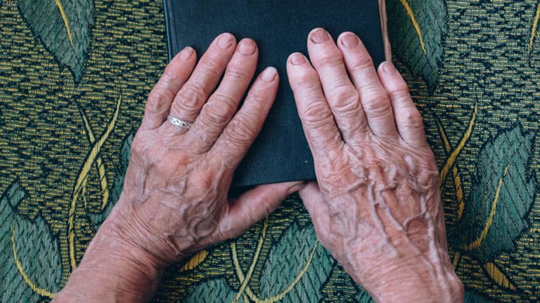 Senior hands on a book on table