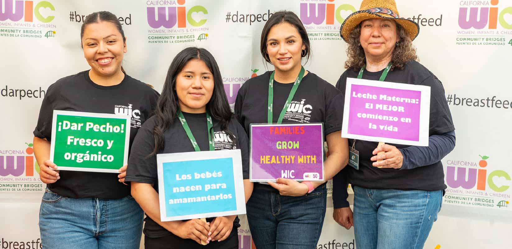 Four women with signs in front of WIC banner